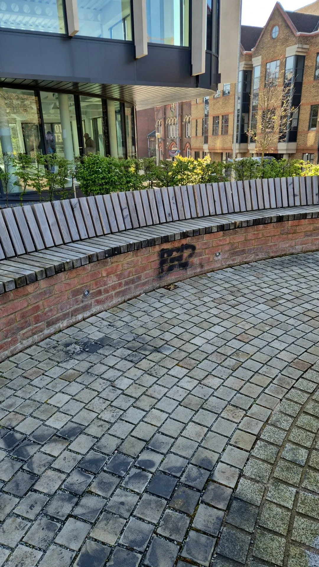 Black spray paint graffiti on brick wall beneath public bench