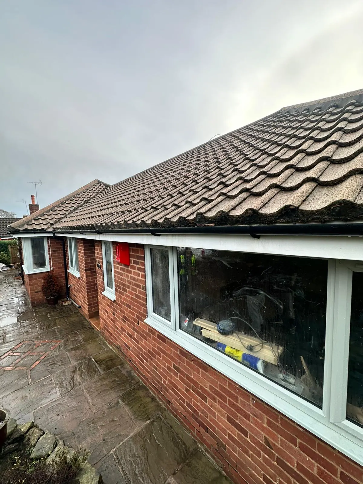 Bungalow roof before professional cleaning showing heavy moss build-up along the tile edges and gutters