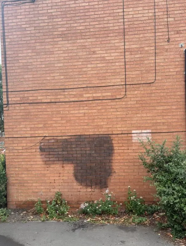 Black spray paint graffiti covering large area of red brick wall
